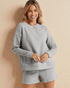 Woman wearing a gray sweatshirt and shorts set against a beige background