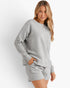 A woman modeling a light gray textured matching lounge set consisting of a long-sleeve sweatshirt and shorts, posed against a clean white studio background.