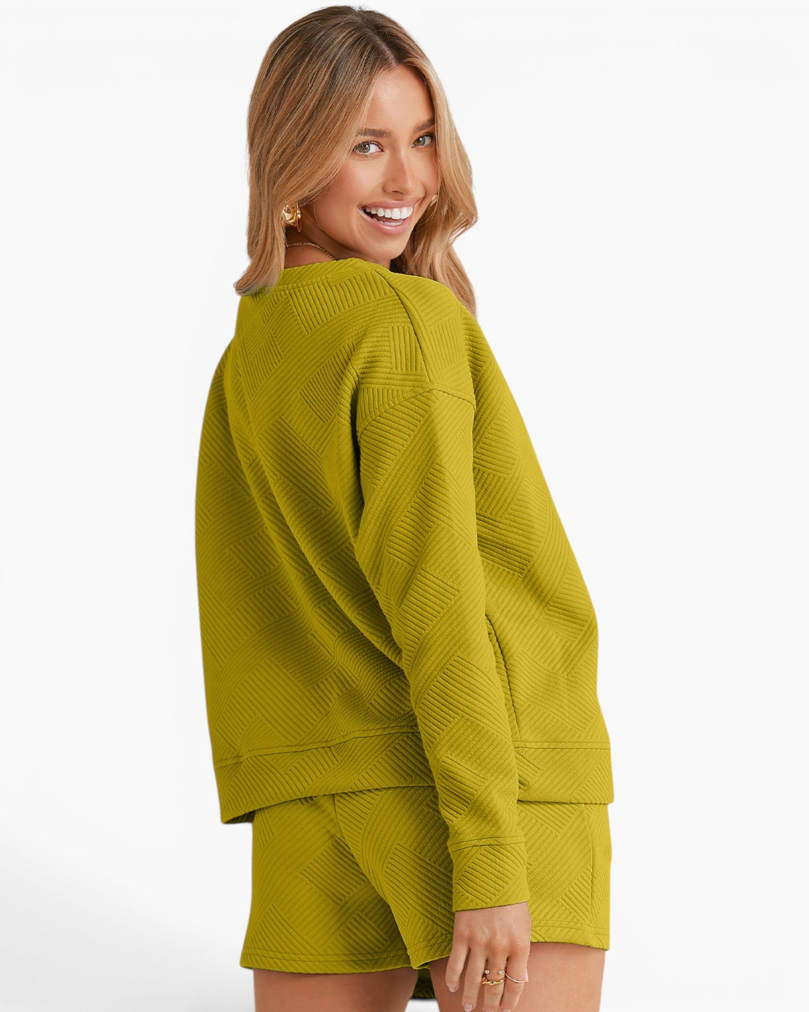 A woman wearing a textured olive green matching lounge set consisting of a long-sleeve top and shorts, photographed against a clean white studio background.