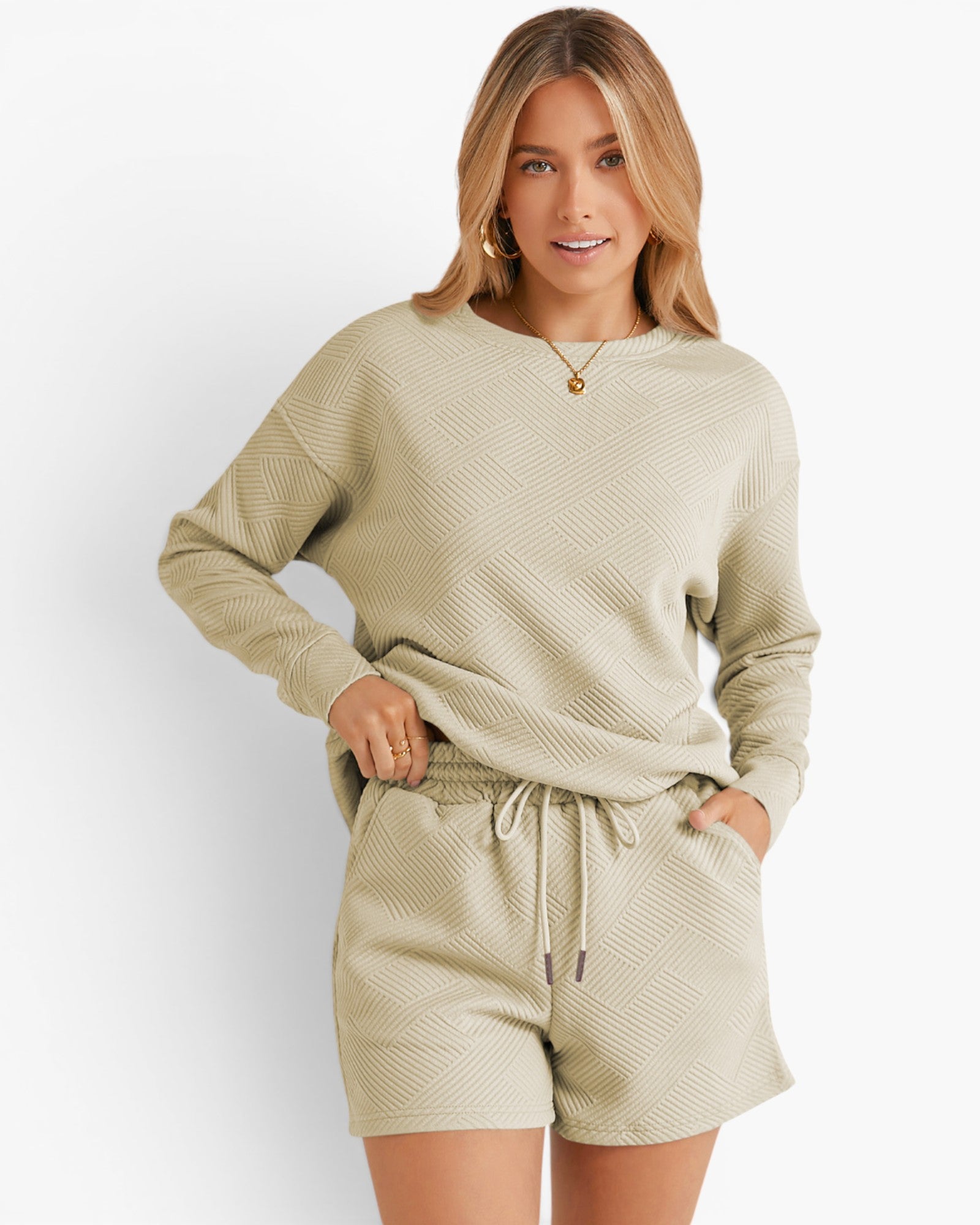 A woman modeling a matching lounge set consisting of a long-sleeve crewneck sweater and drawstring shorts in a light sage green color with a subtle textured chevron pattern, set against a plain white background.