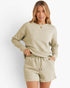 A woman modeling a matching lounge set consisting of a long-sleeve crewneck sweater and drawstring shorts in a light sage green color with a subtle textured chevron pattern, set against a plain white background.