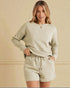Woman wearing a matching beige sweater and shorts set against a beige wall.