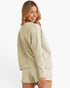 A woman wearing a matching beige textured lounge set consisting of a long-sleeve sweatshirt and shorts, shown from a three-quarters back view against a plain white background.