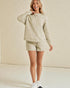 Woman wearing a beige sweatshirt and shorts set on a plain background