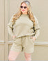 Woman wearing a beige sweatshirt and shorts set against a beige wall.