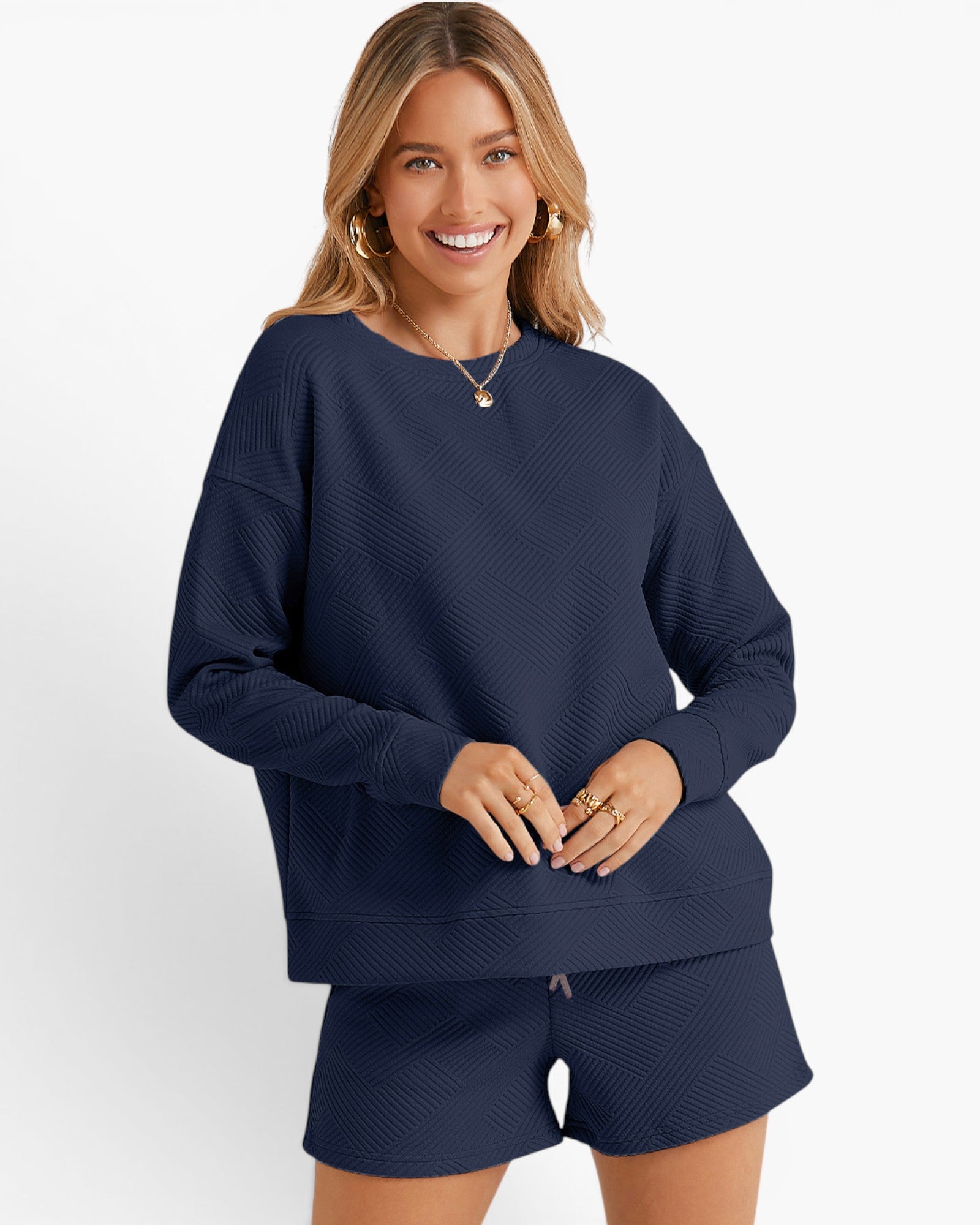 A woman modeling a matching navy blue lounge set featuring a textured knit long-sleeve top and shorts, set against a plain white studio background.