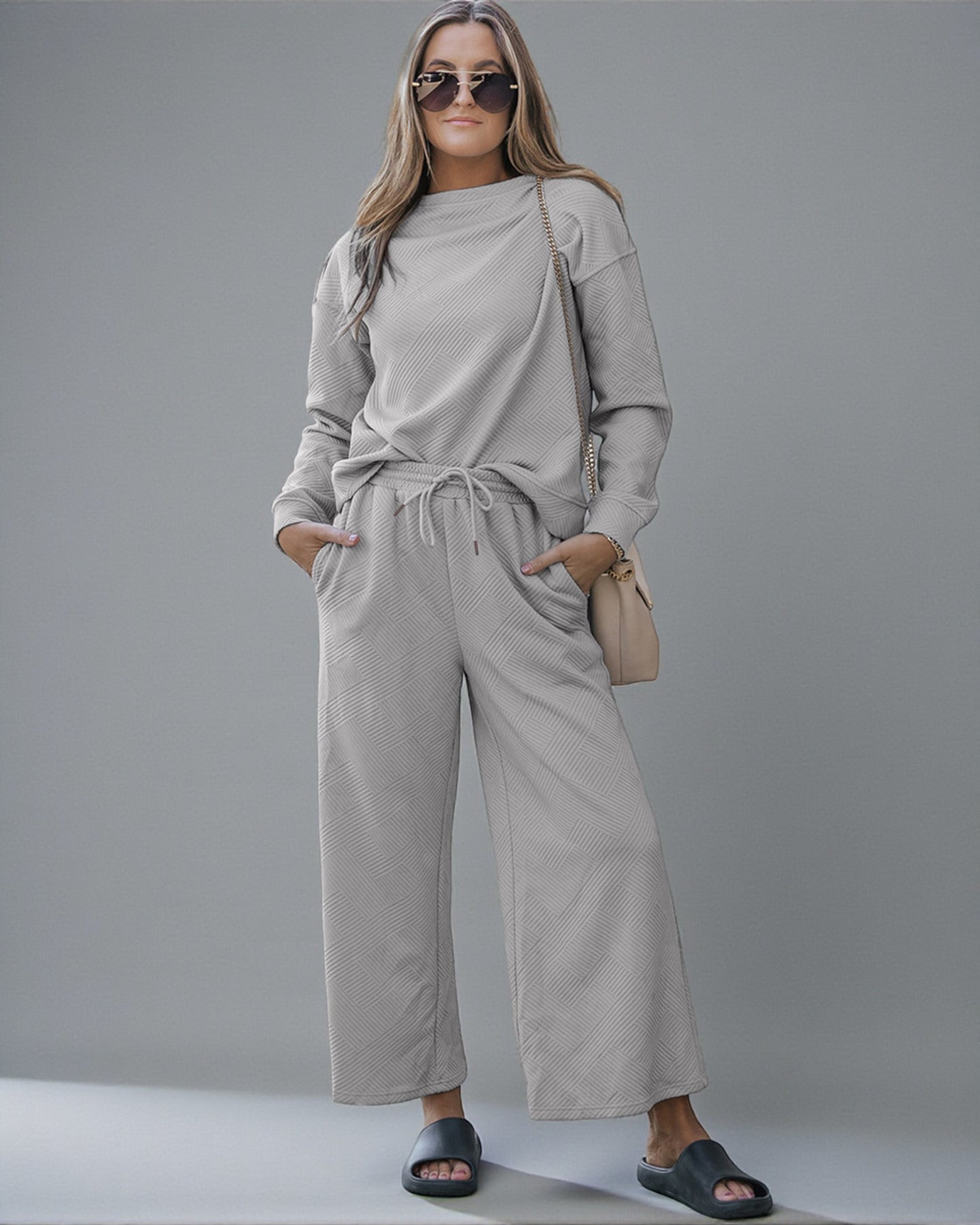 Woman wearing a beige tracksuit with sunglasses and a handbag on a gray background