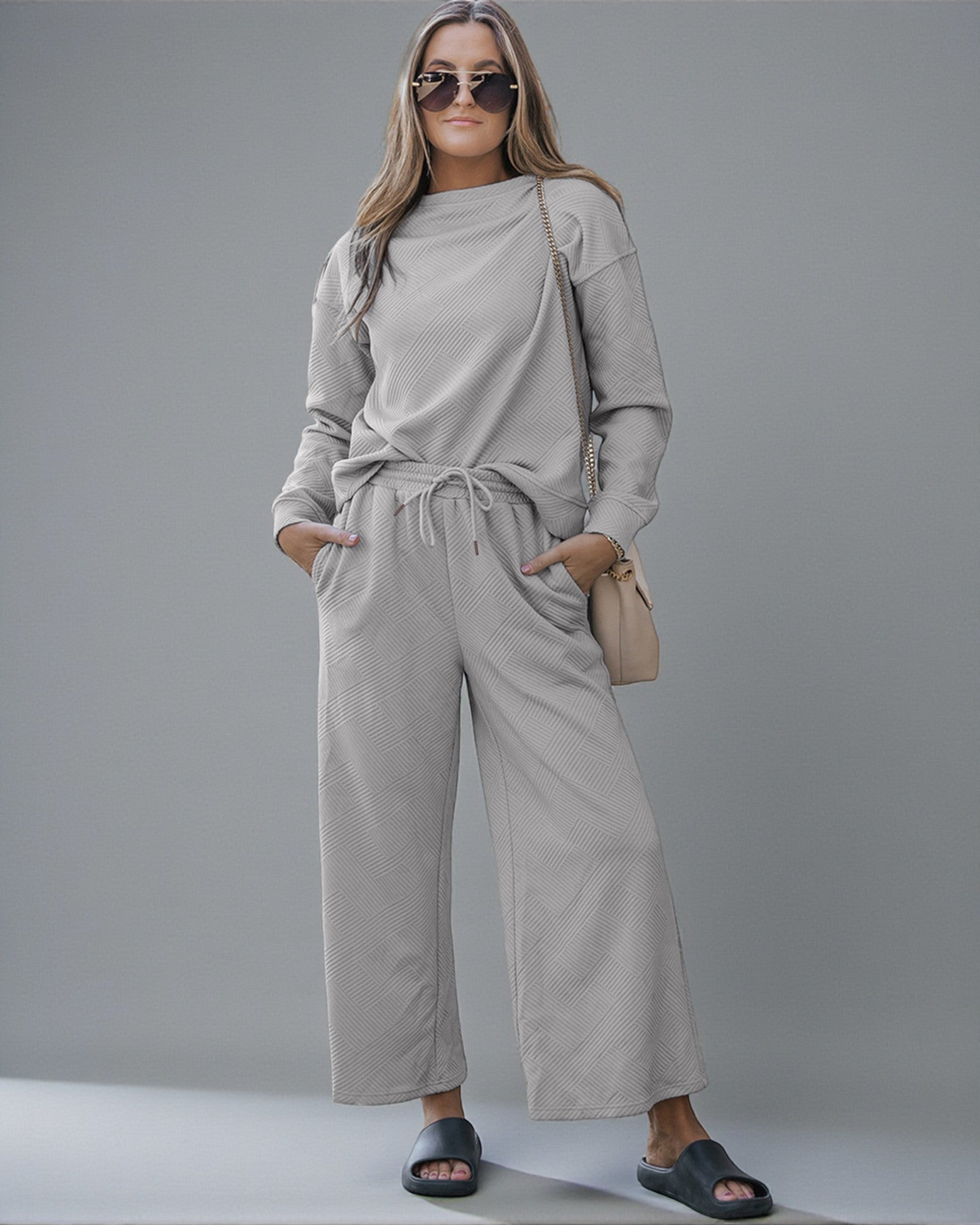 Woman wearing a beige tracksuit with sunglasses and a handbag on a gray background