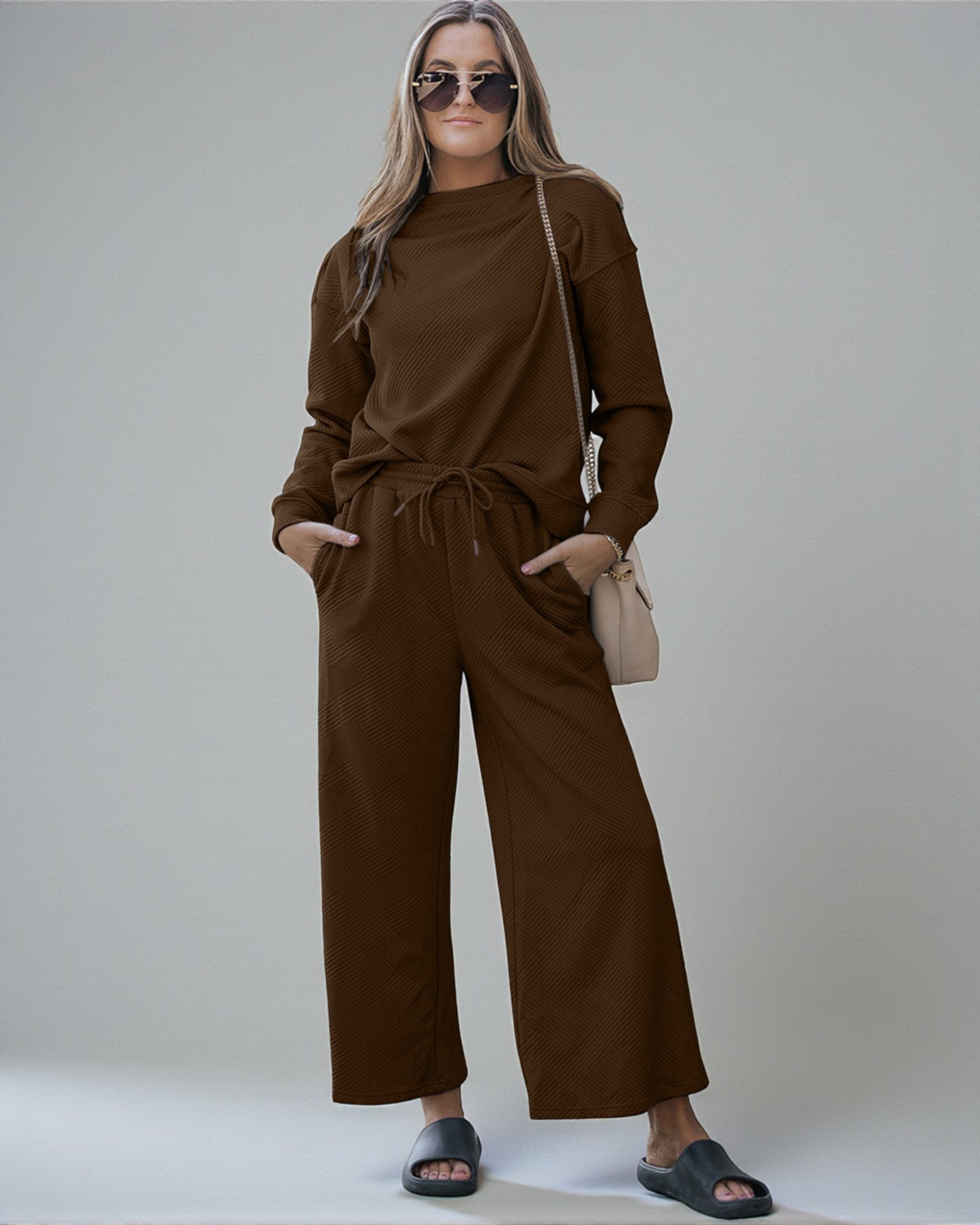 Woman wearing a brown outfit with sunglasses and a beige handbag on a plain background