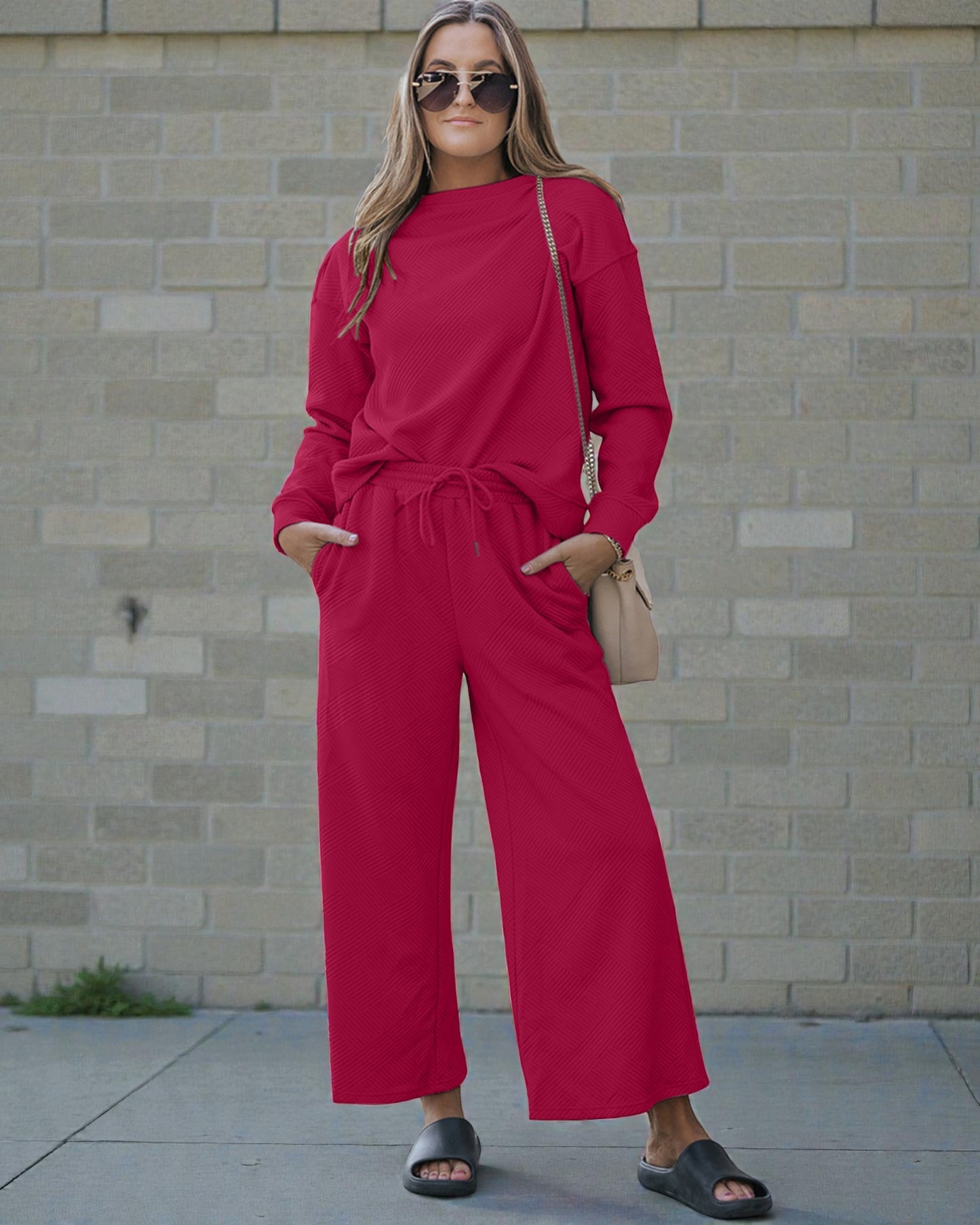 Woman wearing a red outfit standing against a brick wall.