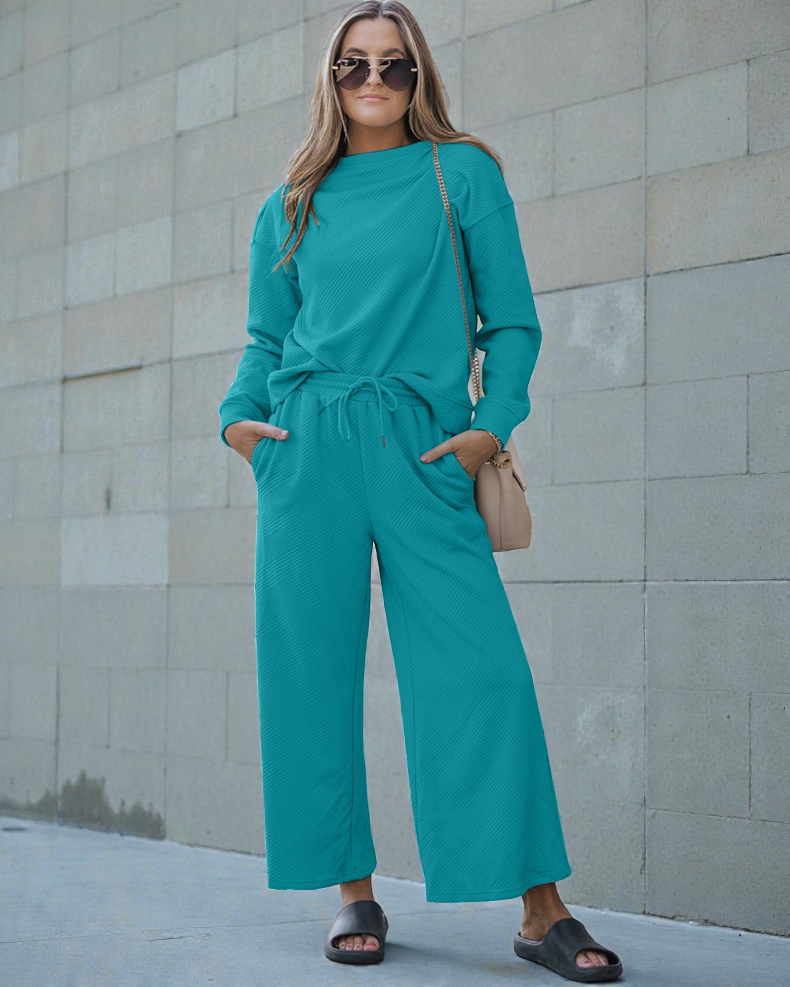 Woman wearing a teal outfit standing against a light stone wall.
