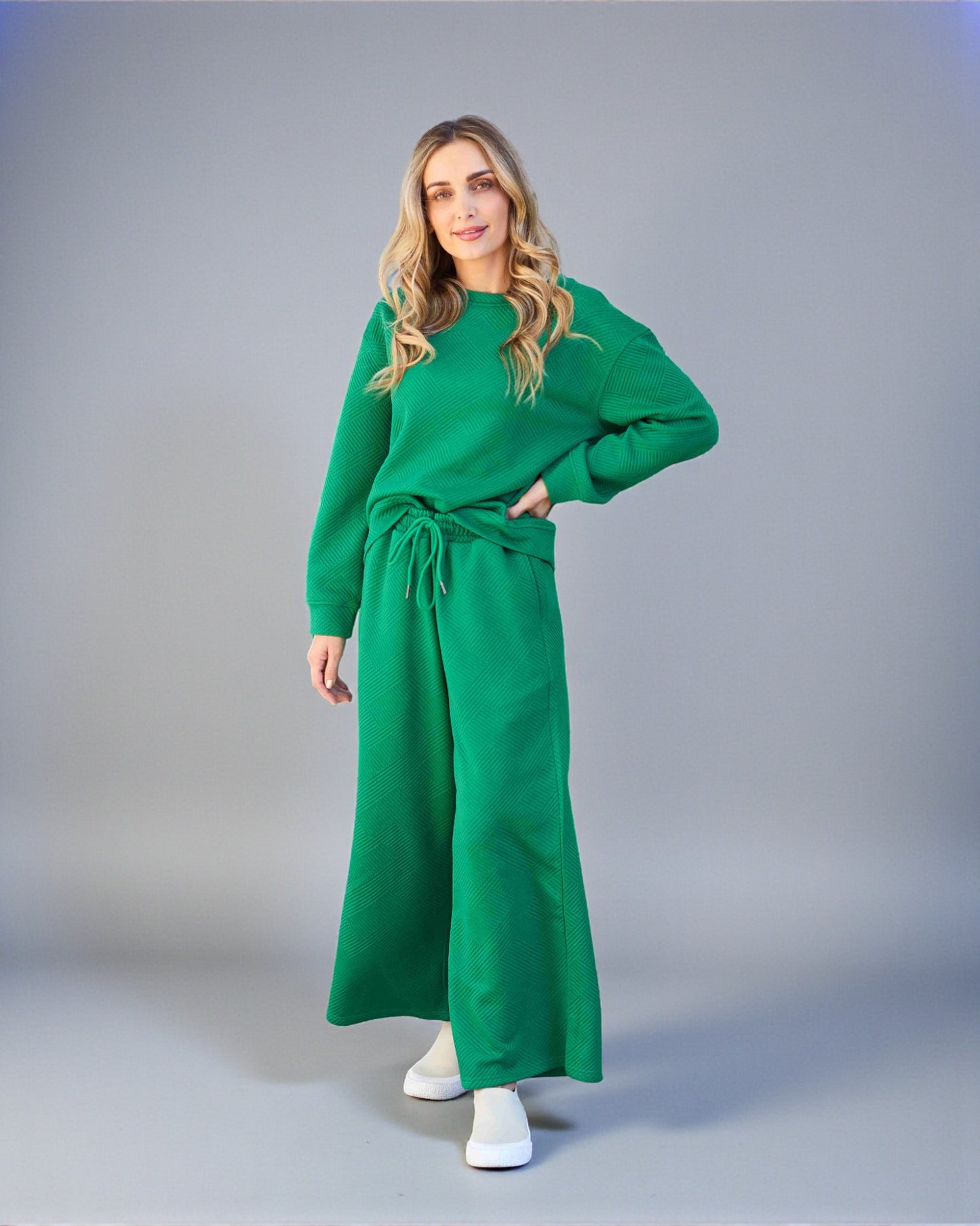 Woman wearing a green outfit with a long dress and sweater on a gray background