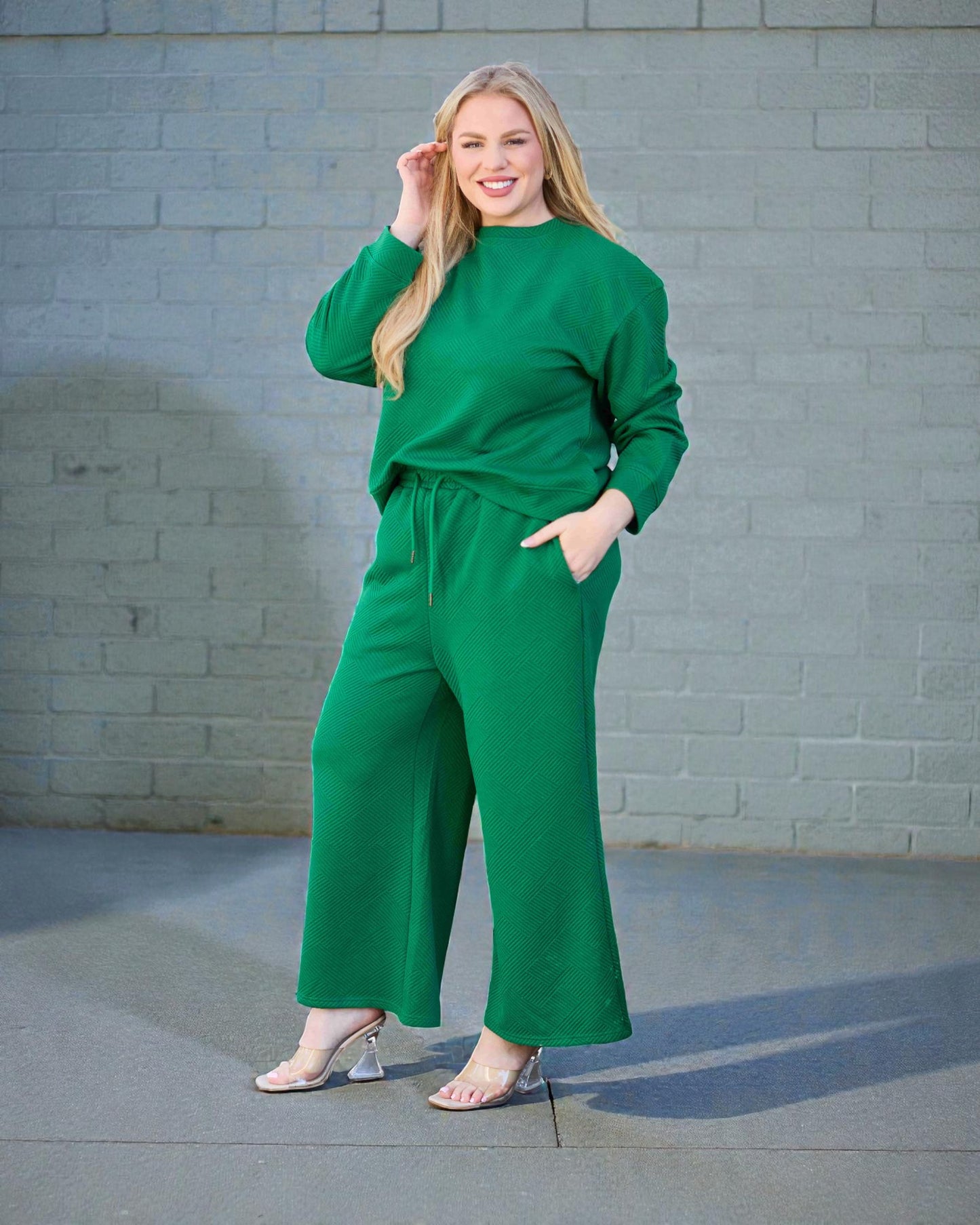 Woman wearing a green outfit standing against a gray brick wall.