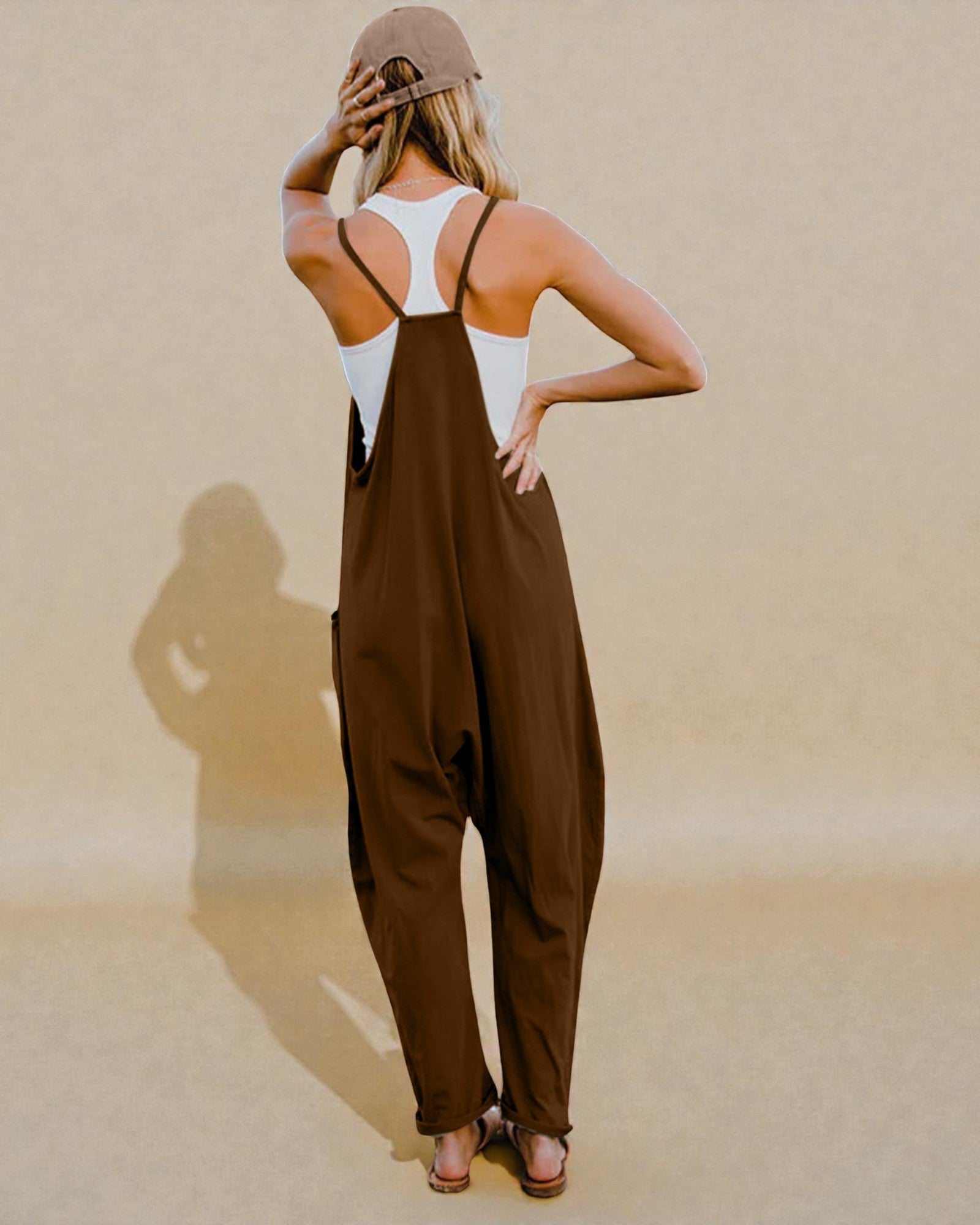 Woman wearing a brown jumpsuit and beige cap against a beige background