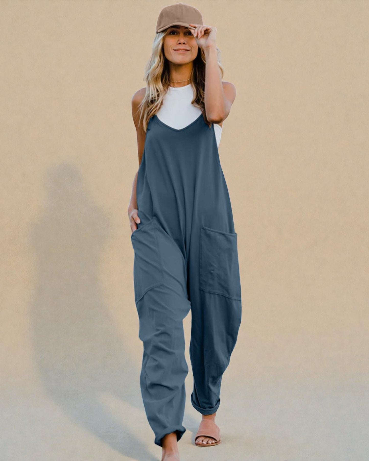 Woman wearing a blue jumpsuit and beige cap against a beige background