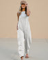 Woman wearing a white sleeveless jumpsuit against a beige wall.
