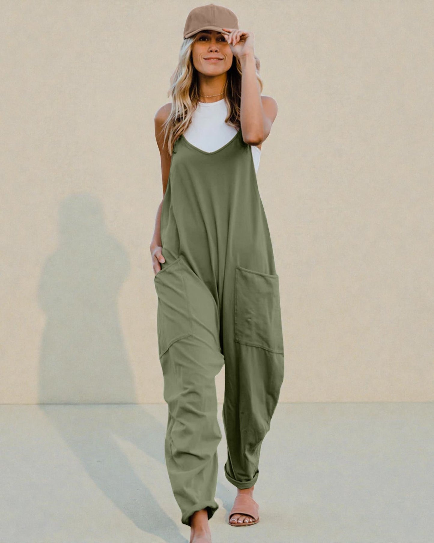 Woman wearing an olive green jumpsuit with a beige cap against a plain background