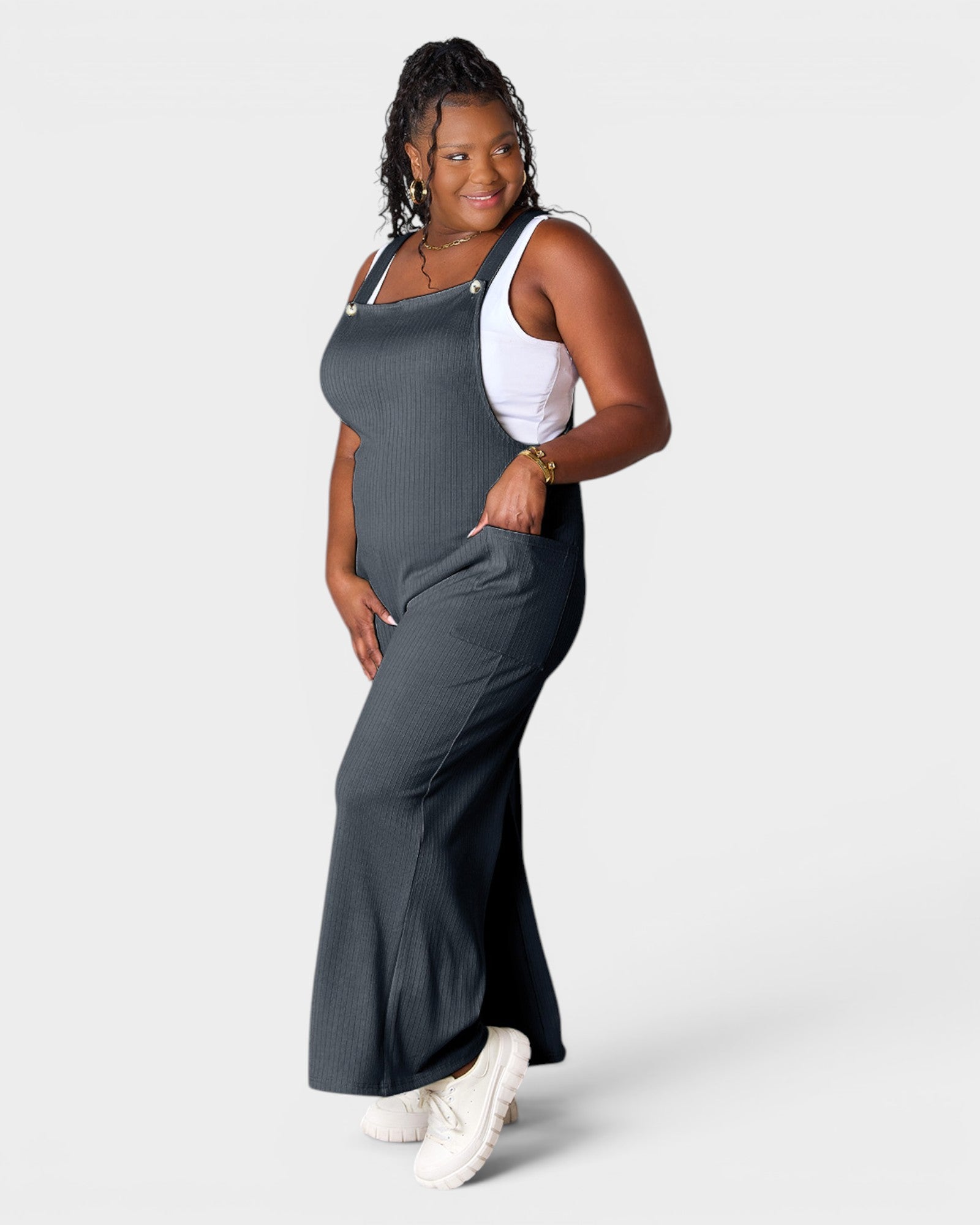 Woman wearing a gray dress overalls with a white top on a plain background
