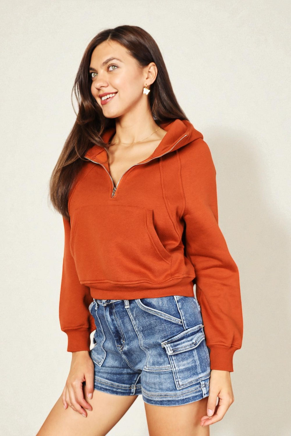 Woman wearing a rust-colored hoodie and denim shorts against a plain background