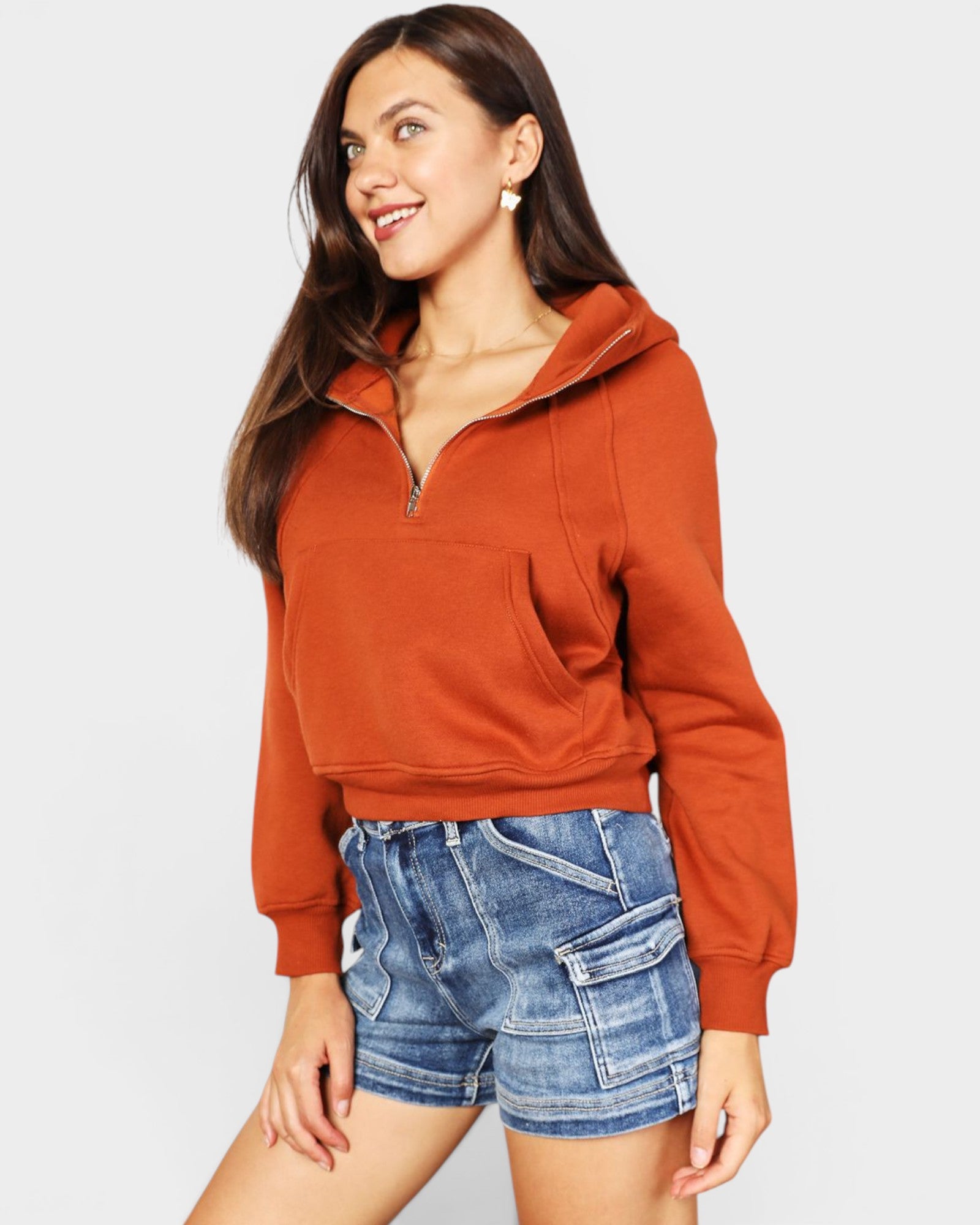 Woman wearing a rust-colored hoodie and denim shorts on a light gray background