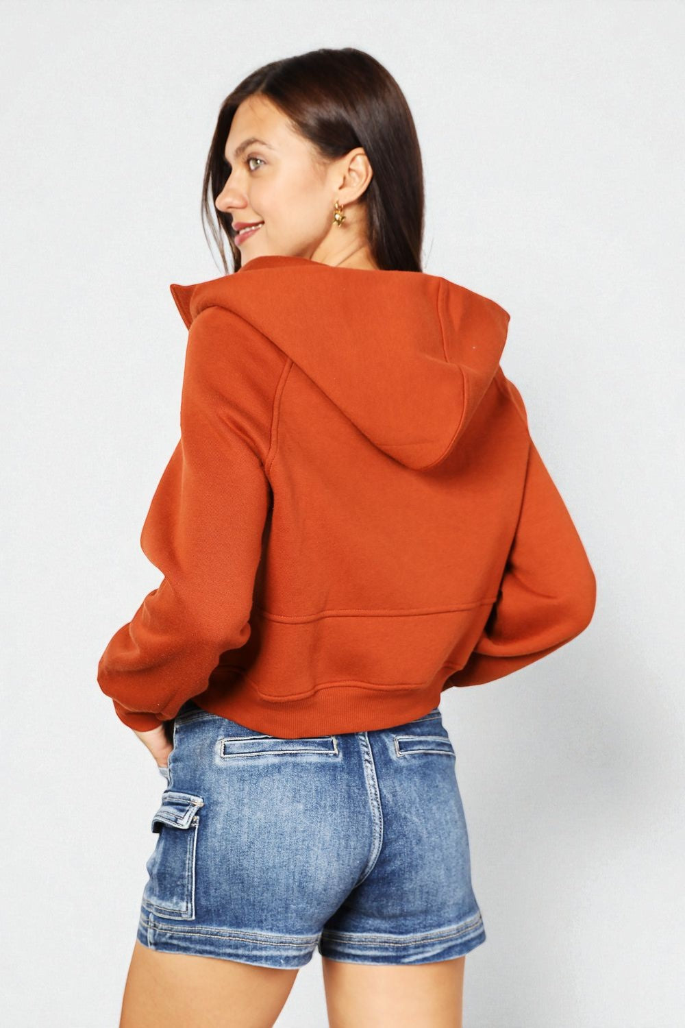 Person wearing a rust-colored hoodie and blue shorts on a white background