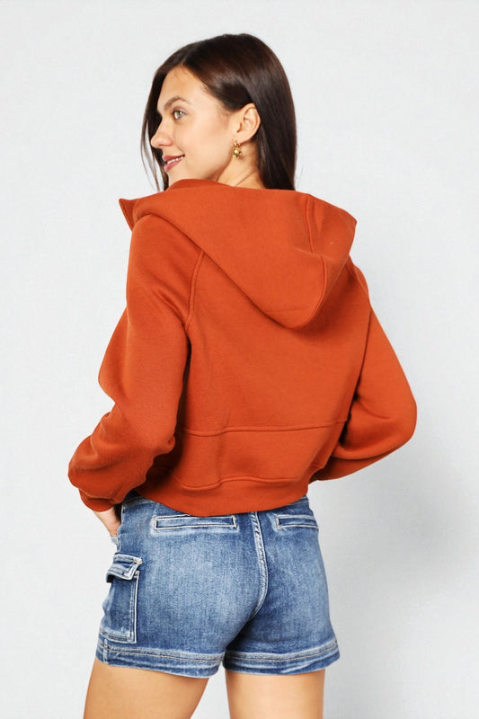 Person wearing a rust-colored hoodie and blue shorts on a white background