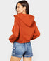 Person wearing a rust-colored hoodie and blue denim shorts on a white background