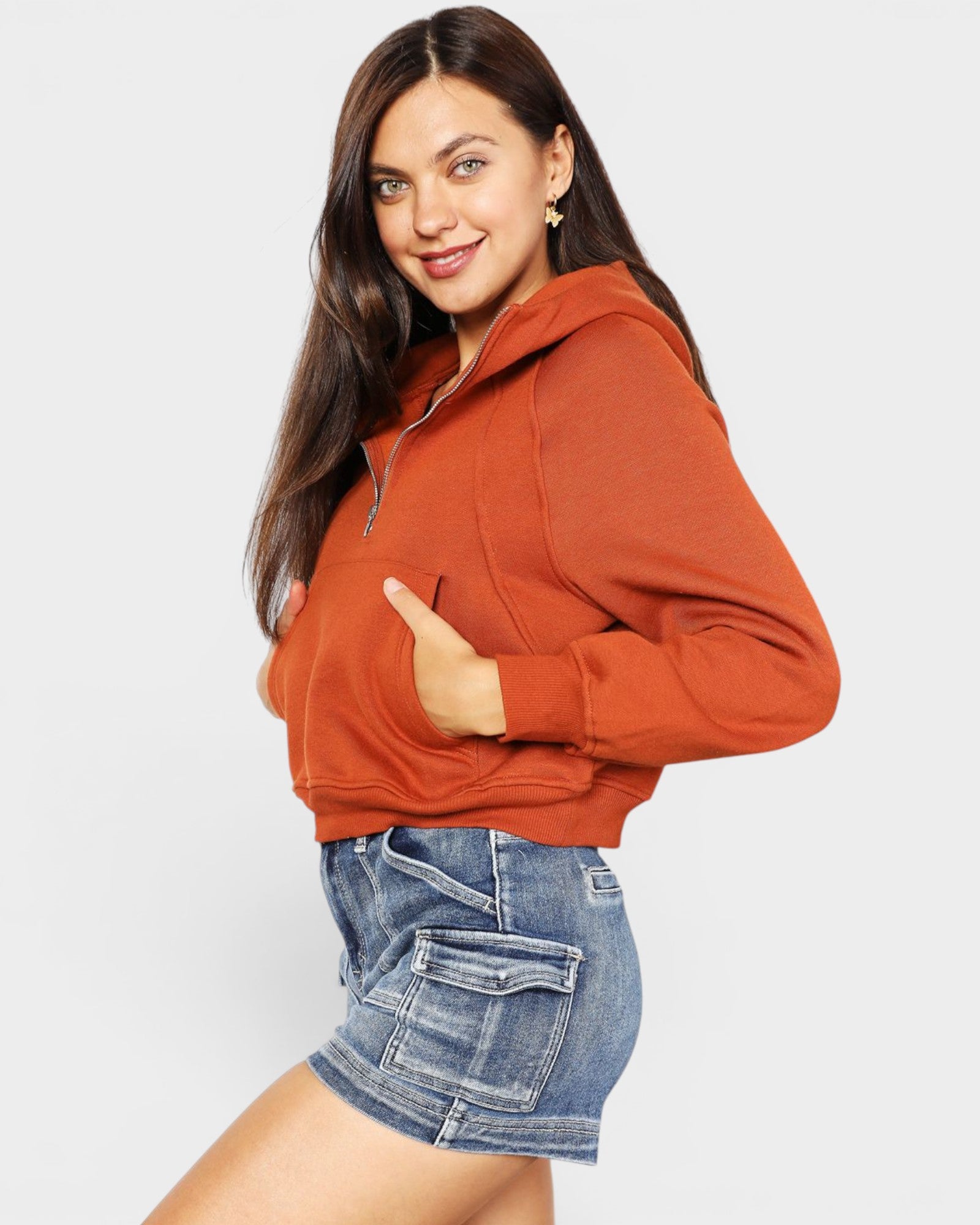 Woman wearing a rust-colored hoodie and denim shorts on a light gray background