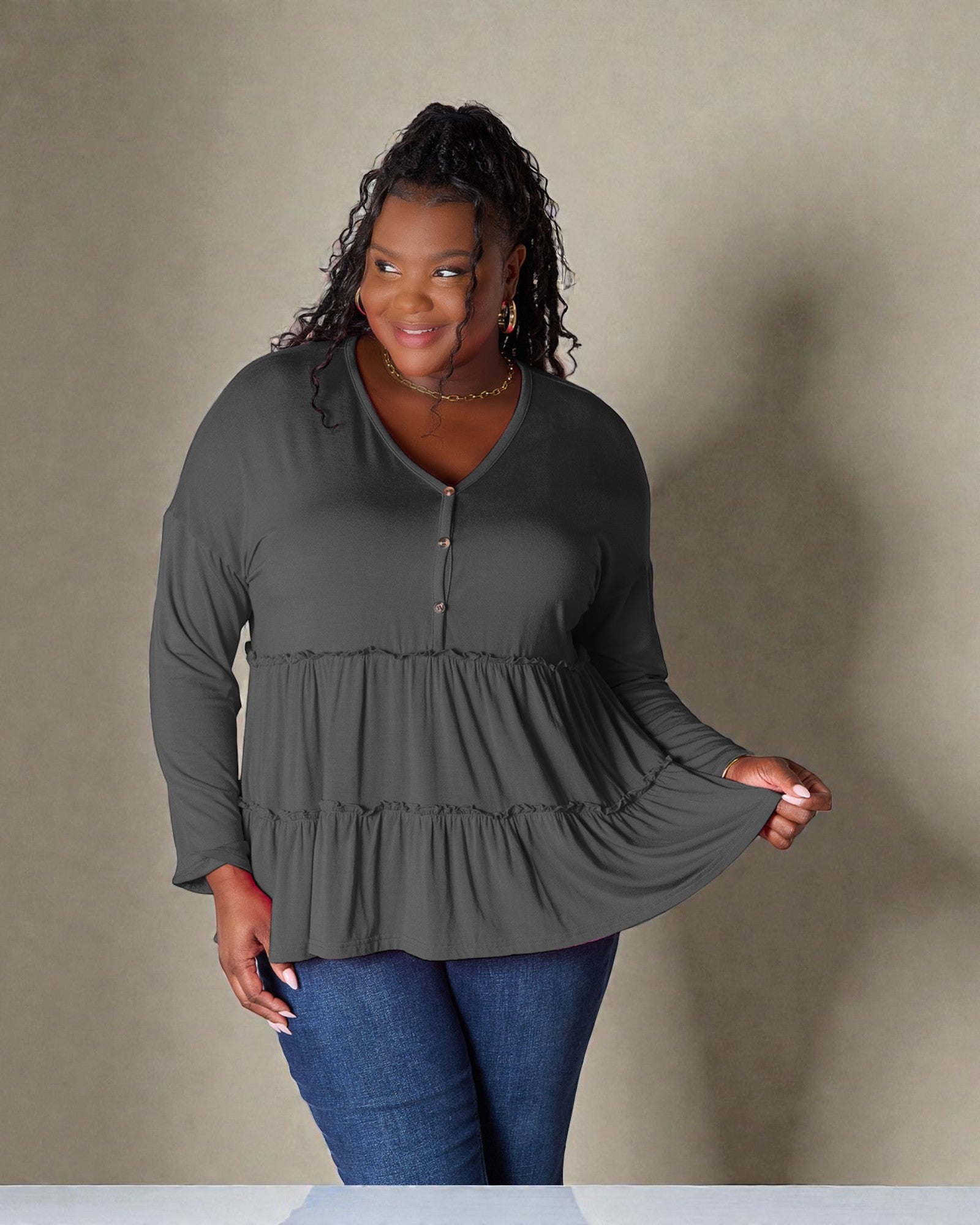 Woman wearing a gray long-sleeve top with a ruffled design against a beige background