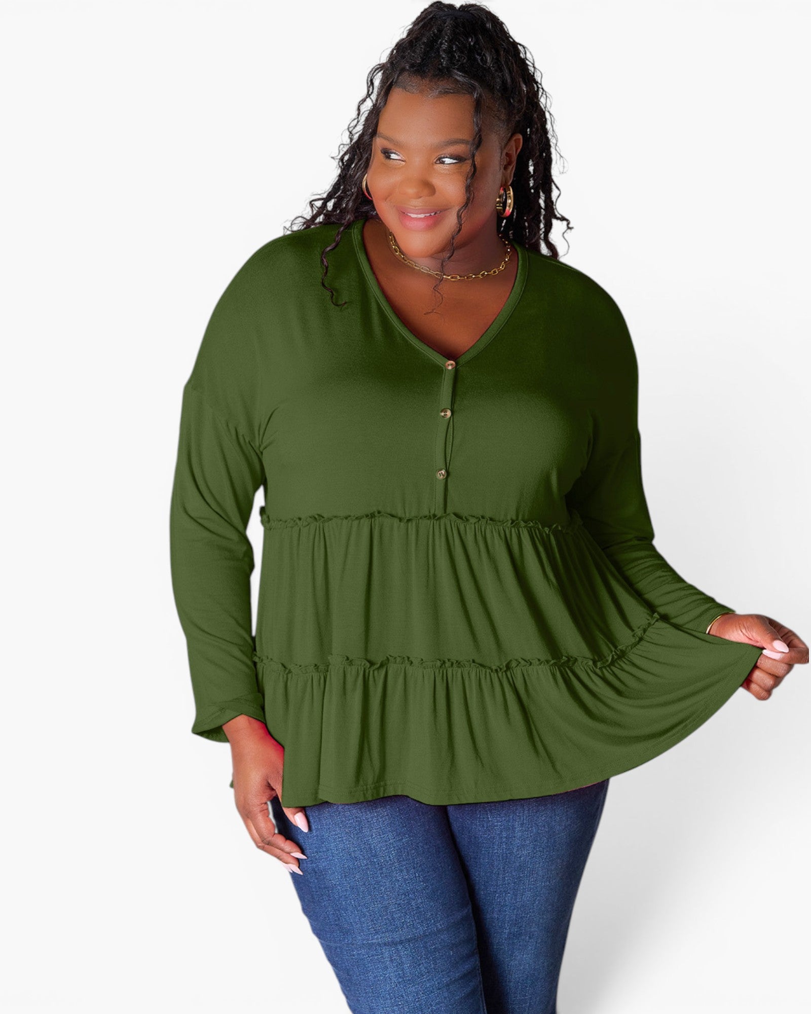 A woman modeling a long-sleeve olive green tiered blouse with a buttoned V-neckline, paired with blue jeans, against a plain white studio background.
