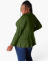 A woman wearing a sage green long-sleeve top with a tiered ruffle hem, shown from a back-three-quarter angle against a plain white background.