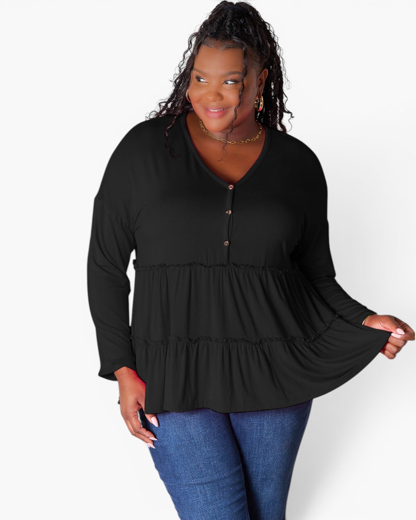 A woman modeling a black long-sleeve peplum top with a buttoned neckline, paired with blue jeans, against a plain white studio background.