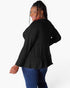 A woman modeling a black long-sleeve top with a tiered ruffle hem, shown from a back-three-quarter angle against a plain white background.