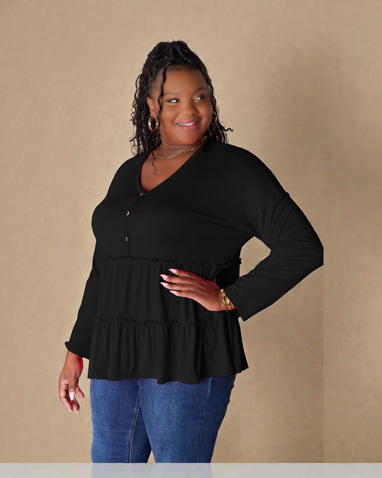 Woman wearing a black long-sleeve top with a ruffled bottom against a beige background