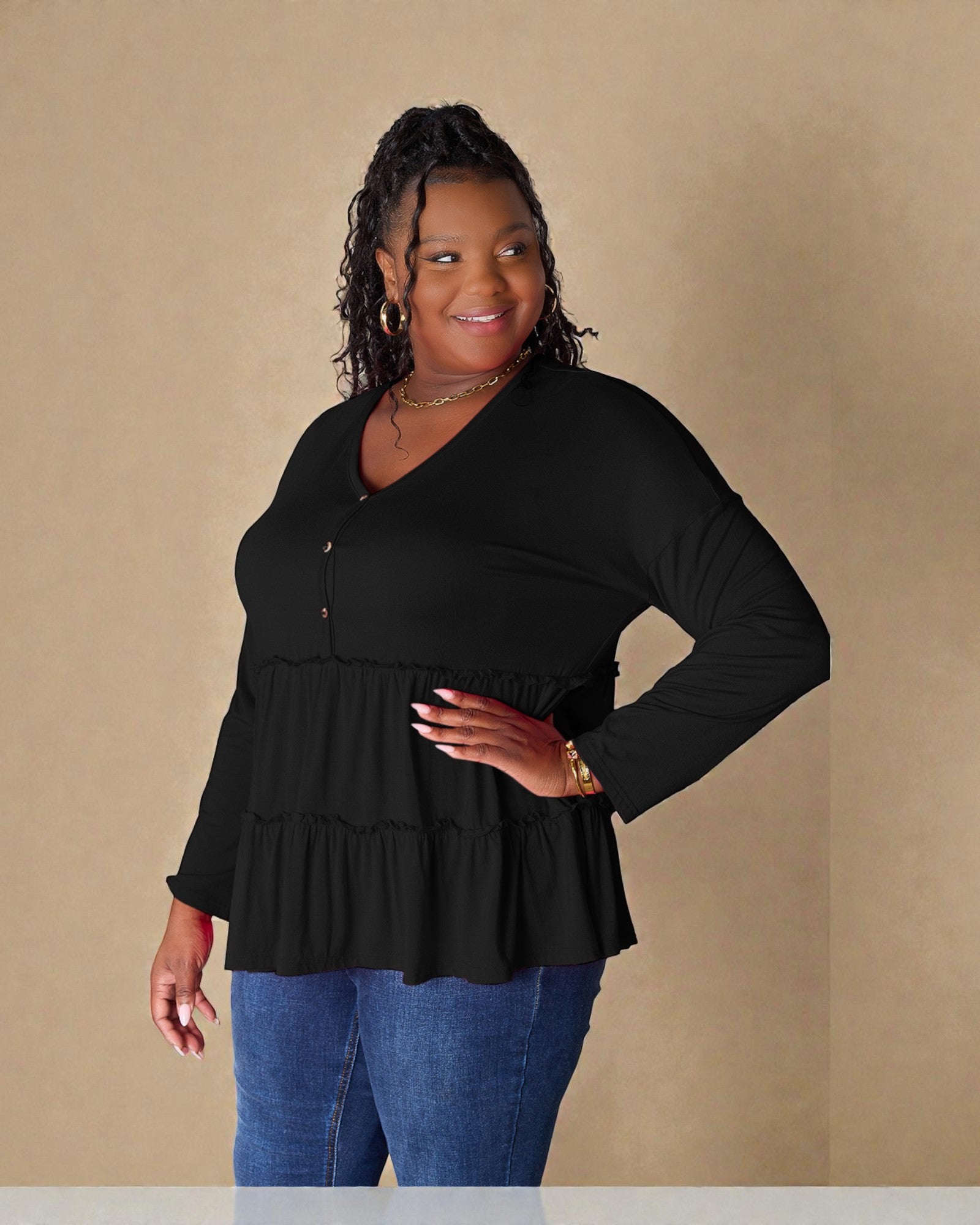Woman wearing a black long-sleeve top with a ruffled bottom against a beige background