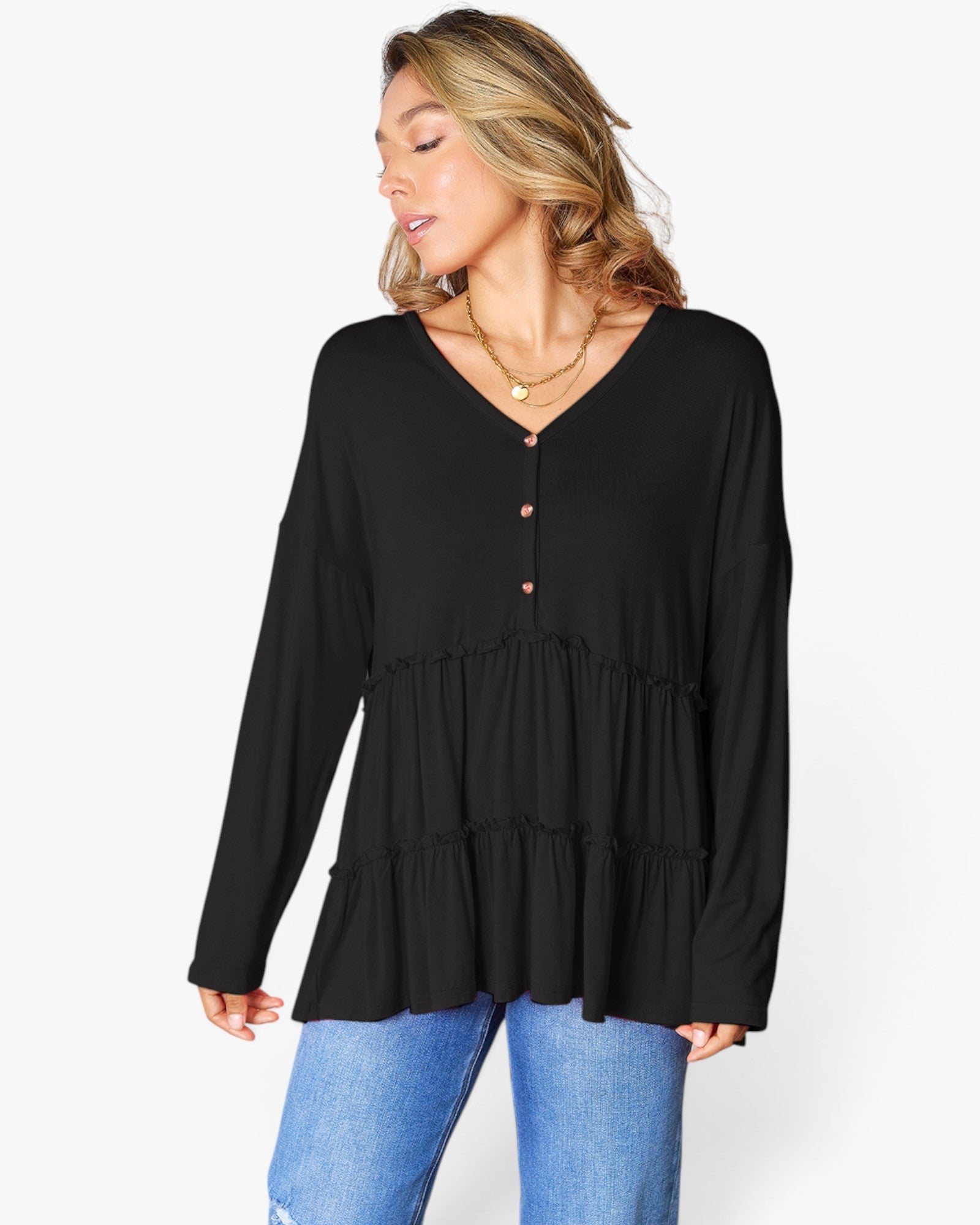 A woman wearing a black long-sleeve tiered blouse with a buttoned V-neckline, paired with blue jeans, photographed against a plain white studio background.