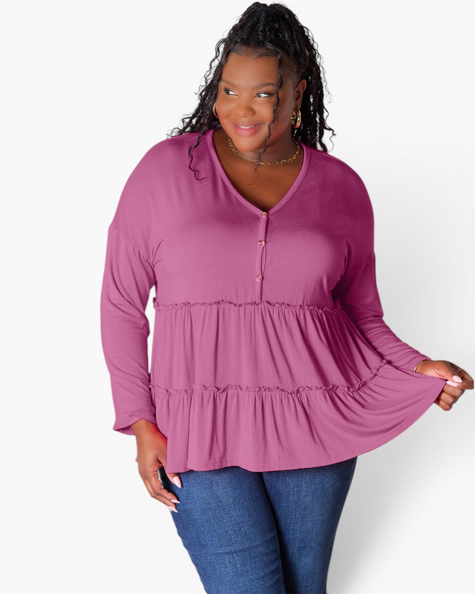 A woman modeling a long-sleeve V-neck blouse in dusty rose pink, paired with blue jeans, against a plain white studio background.
