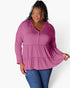 A woman modeling a long-sleeve V-neck blouse in dusty rose pink, paired with blue jeans, against a plain white studio background.