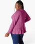 A woman wearing a magenta long-sleeve top and blue jeans, photographed from the back against a light gray studio background.