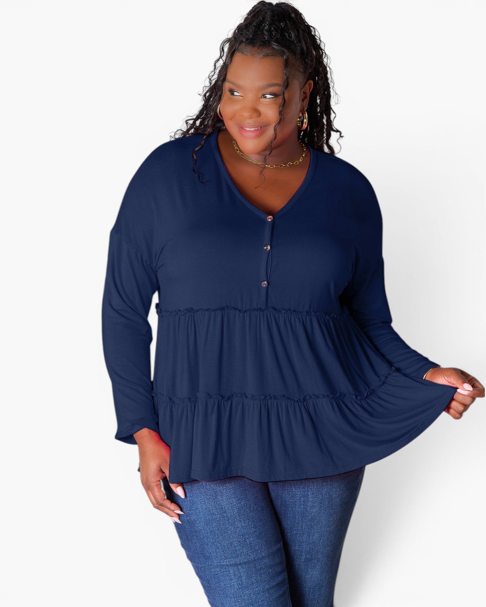 A woman modeling a navy blue long-sleeve peplum top with a buttoned V-neckline, paired with blue jeans, against a plain white studio background.