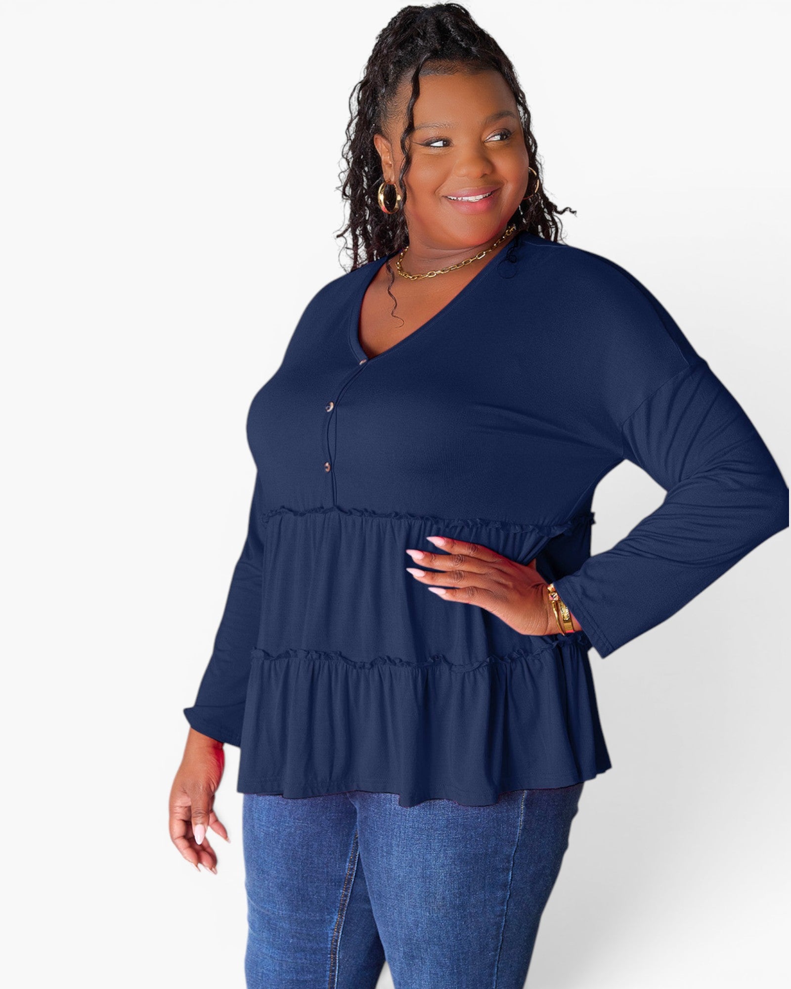 A woman modeling a navy blue long-sleeve top with a tiered peplum hem and button detail at the neckline, paired with blue jeans against a plain white background.