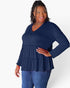 A woman modeling a navy blue long-sleeve top with a tiered peplum hem and button detail at the neckline, paired with blue jeans against a plain white background.