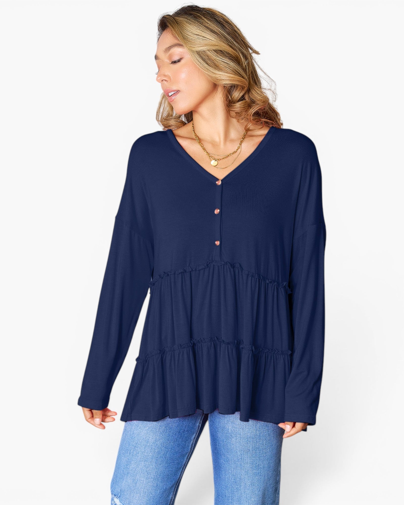 A woman wearing a navy blue long-sleeve tiered blouse with a buttoned V-neckline, paired with light blue jeans, photographed against a clean white studio background.