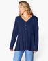 A woman wearing a navy blue long-sleeve tiered blouse with a buttoned V-neckline, paired with light blue jeans, photographed against a clean white studio background.
