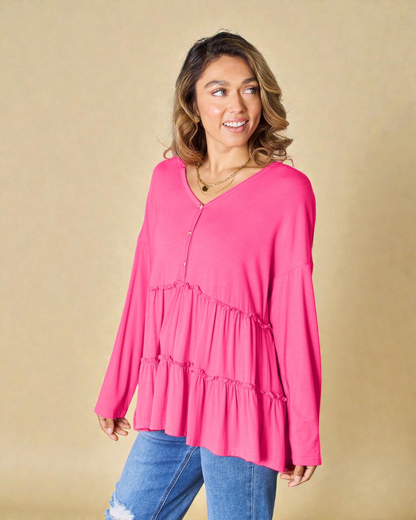 Woman wearing a bright pink long-sleeve top and blue jeans against a beige background