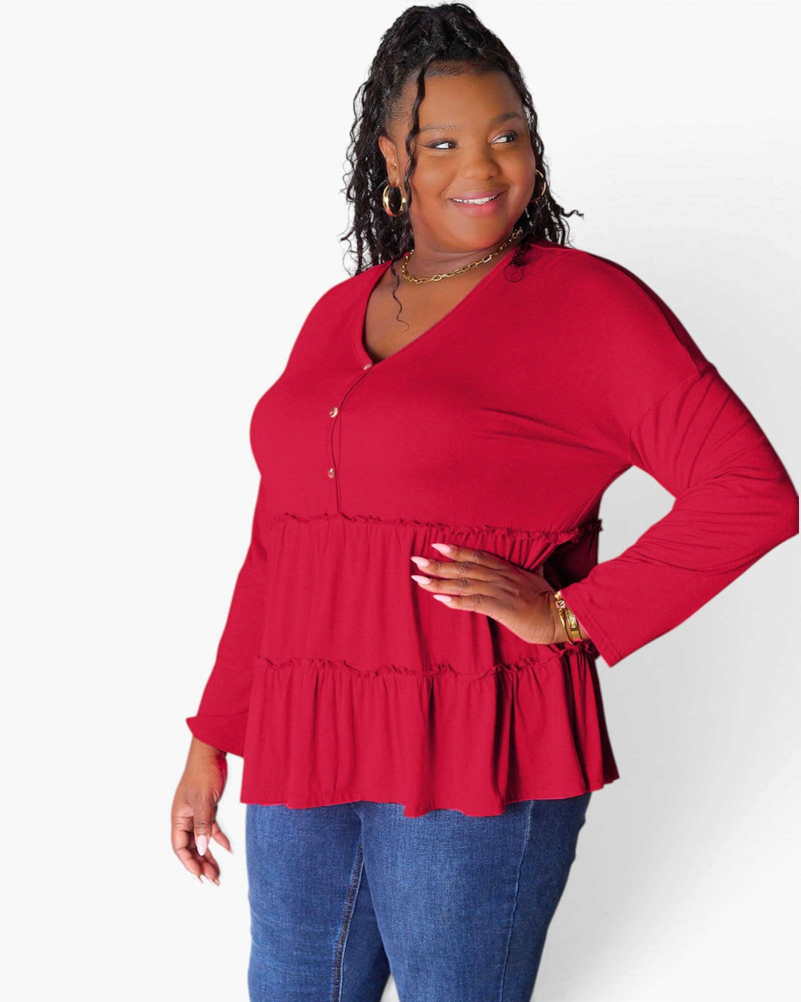 A woman modeling a bright red long-sleeve top with a tiered peplum hem and button placket, paired with blue jeans, against a plain white studio background.