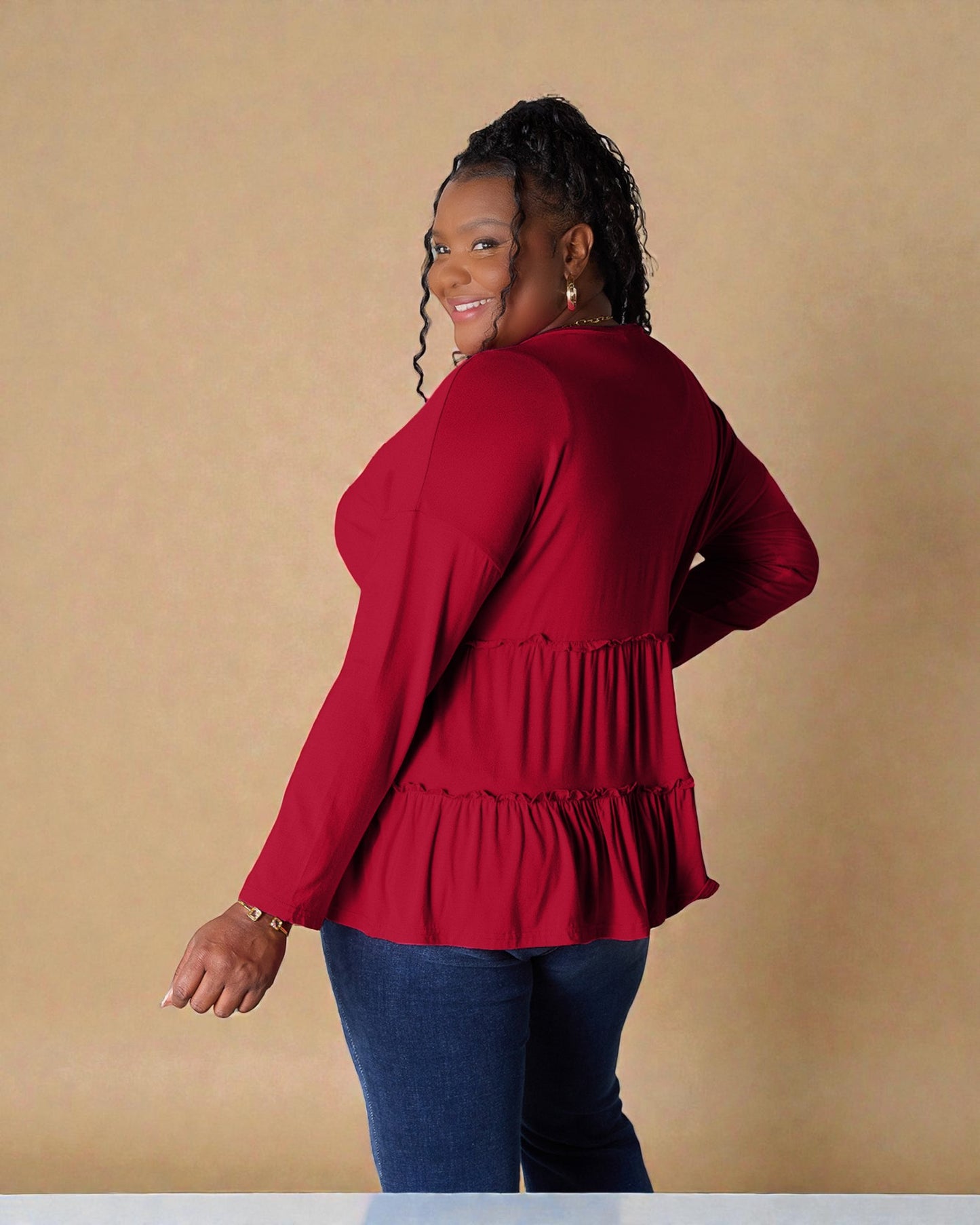 Woman wearing a red peplum top and blue jeans against a beige background