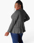 A woman modeling a dark gray long-sleeve top with a tiered ruffle hem, shown from a back-three-quarter angle against a plain white background.