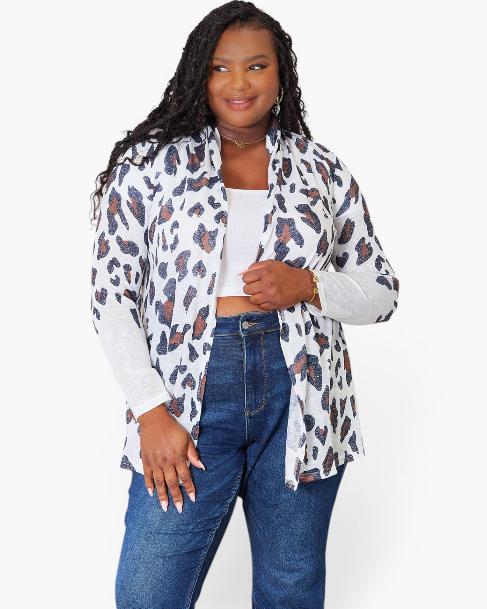 A woman modeling a white long-sleeve button-up shirt with an all-over leopard print pattern in brown and black, worn open over a white crop top and blue jeans, against a plain white background.