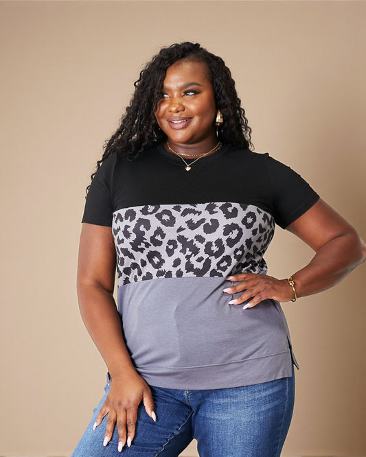 Woman wearing a black, gray, and leopard print shirt with blue jeans on a beige background